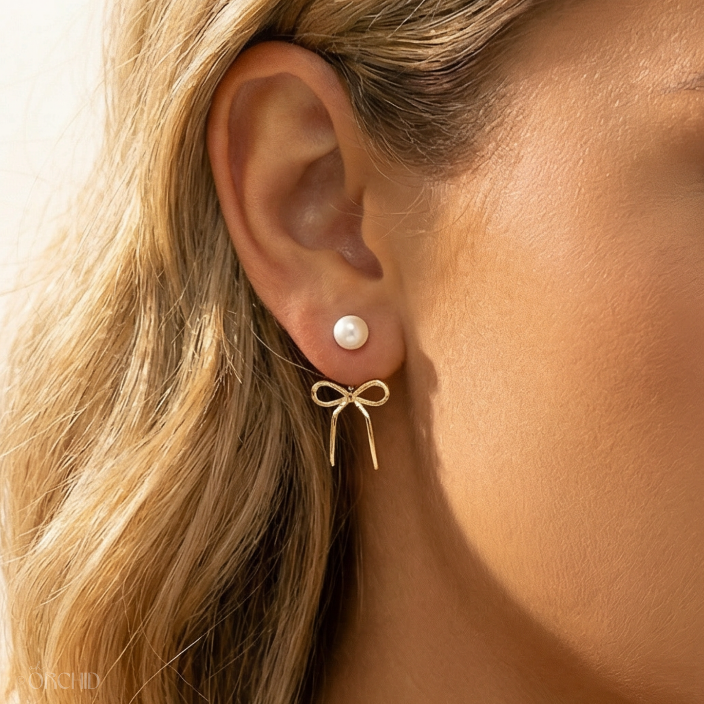 Close-up of an ear wearing a pearl earring with a gold bow detail.