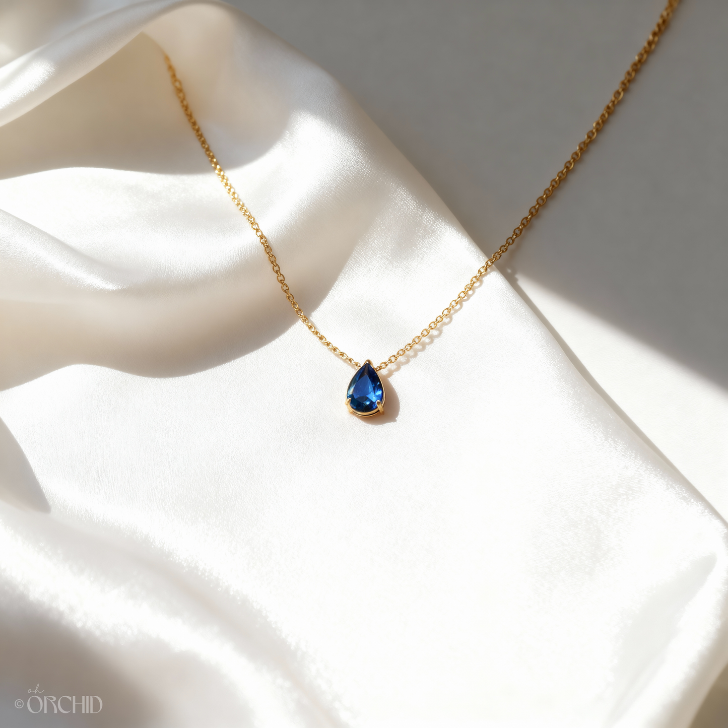 Gold necklace with a blue teardrop pendant on a white fabric background