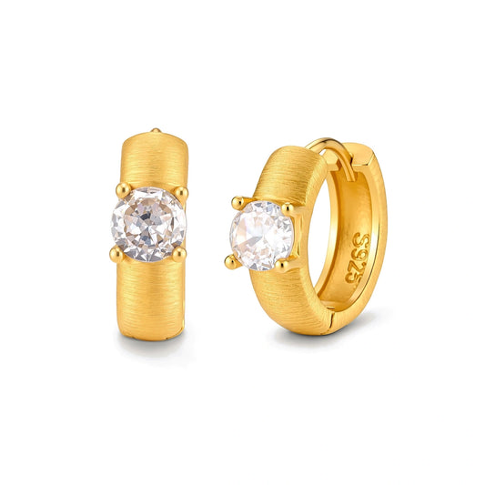 Juno Solitaire Huggies, pair of brushed gold huggie hoops, one seen front-on with a four-prong cubic zirconia, one angled showing the S925 stamp inside the hoop
