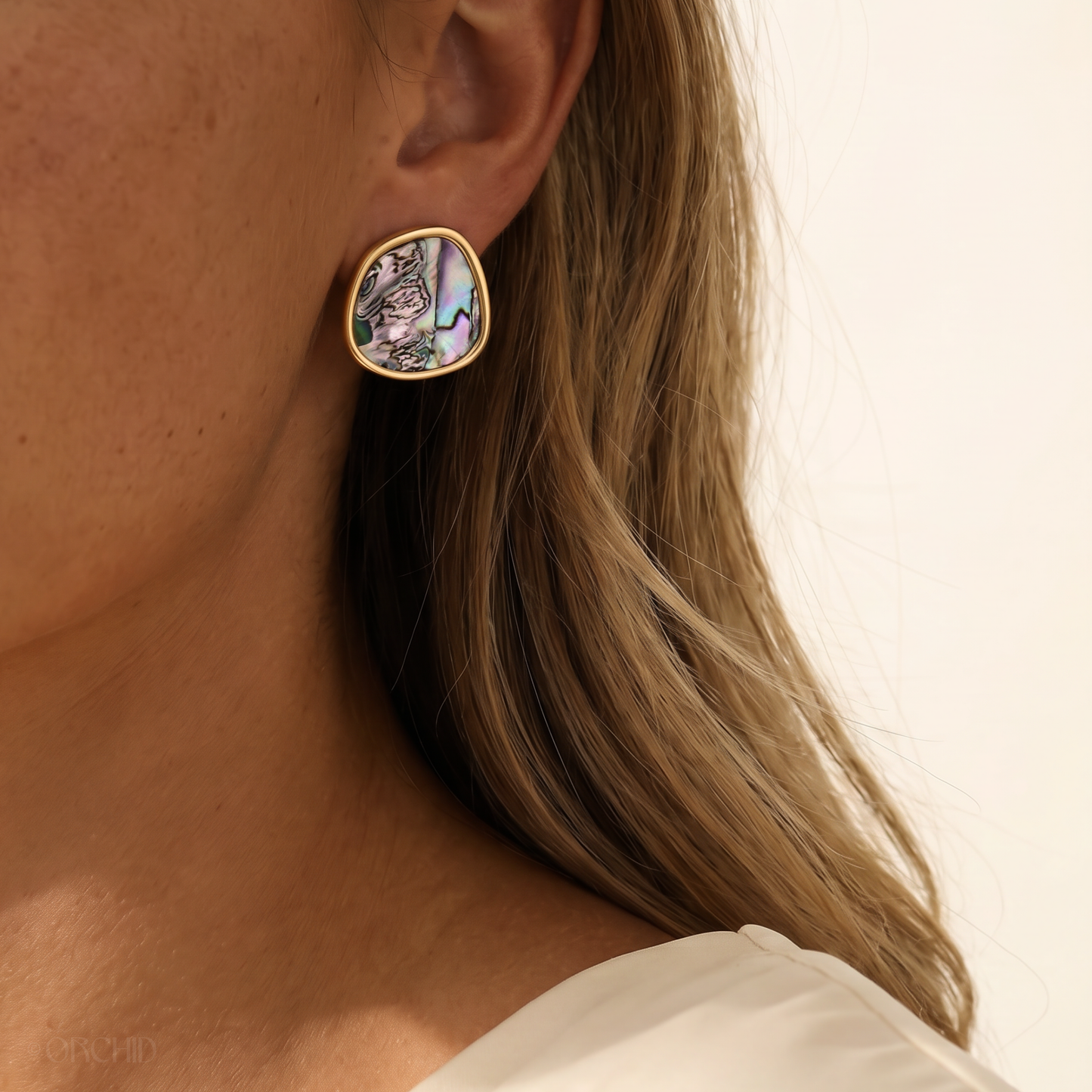 Close-up of a person wearing a gold earring with a colorful abalone stone.