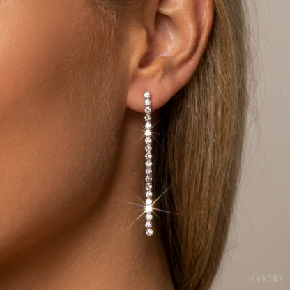 Close-up of an ear wearing a long, sparkling earring against a neutral background.