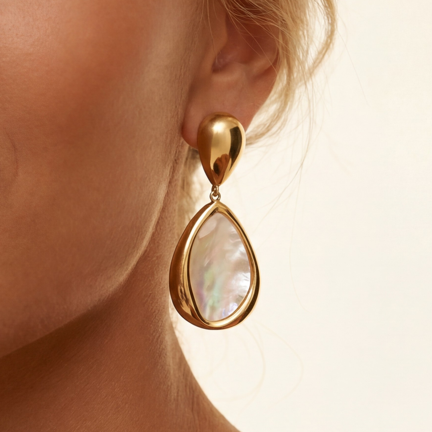 Gold teardrop earring worn by a person with a neutral background