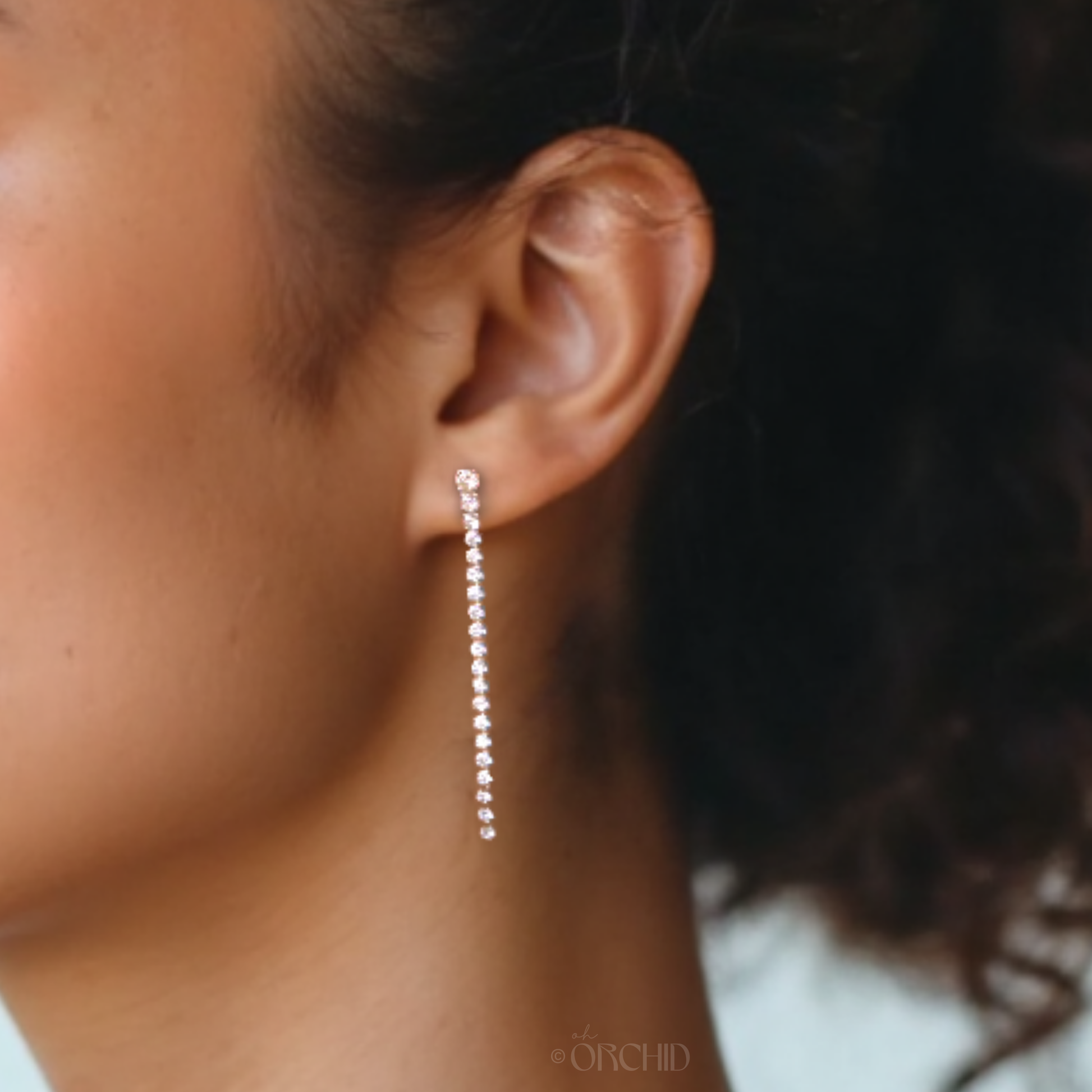 Close-up of an ear wearing a silver chain earring with a blurred background