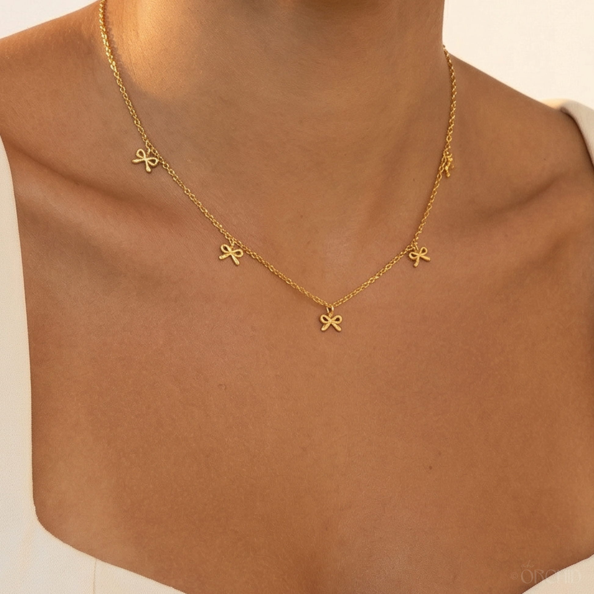 Gold necklace with bow-shaped pendants on a person wearing a brown top.