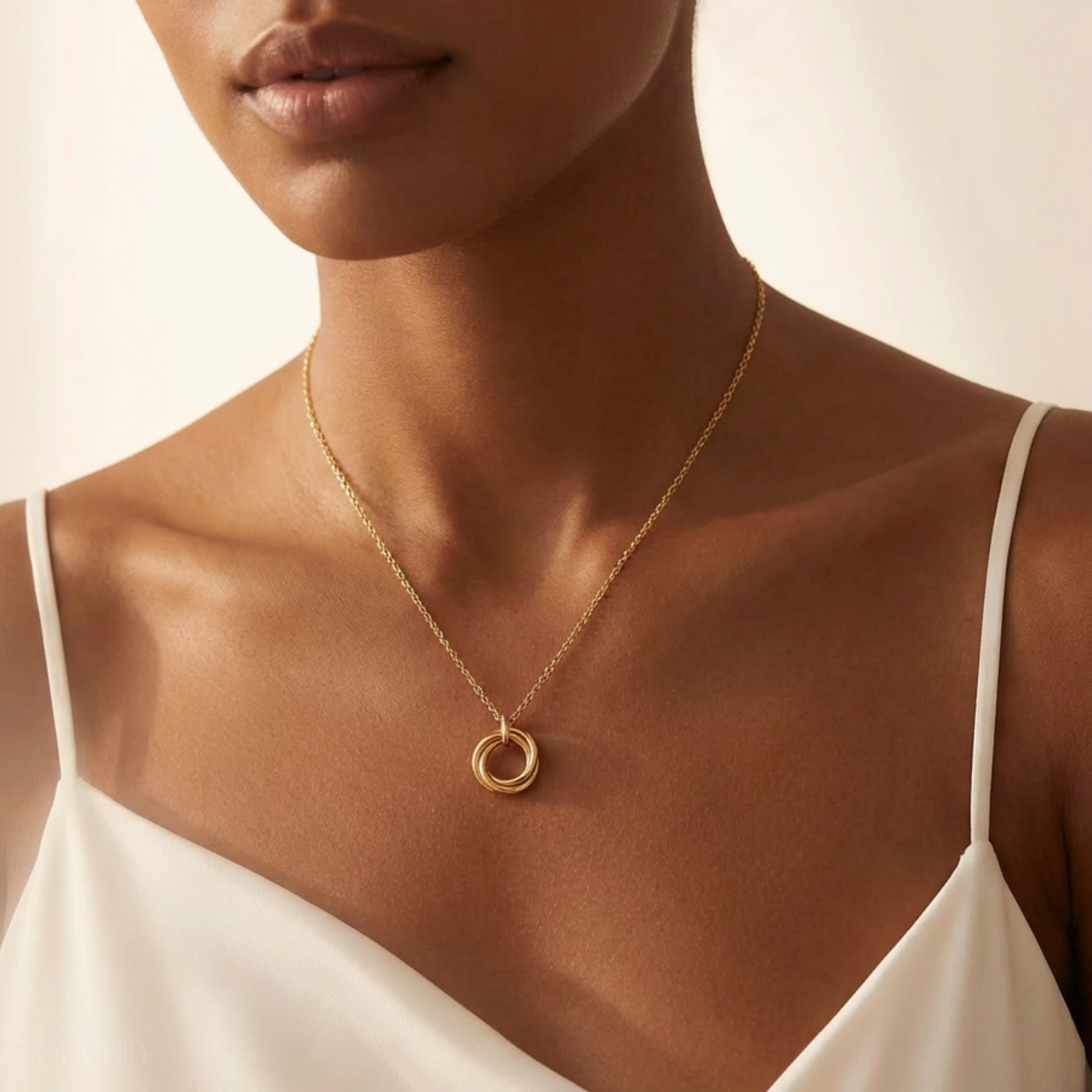 Close-up of a woman wearing a gold necklace with a circular pendant on a neutral background
