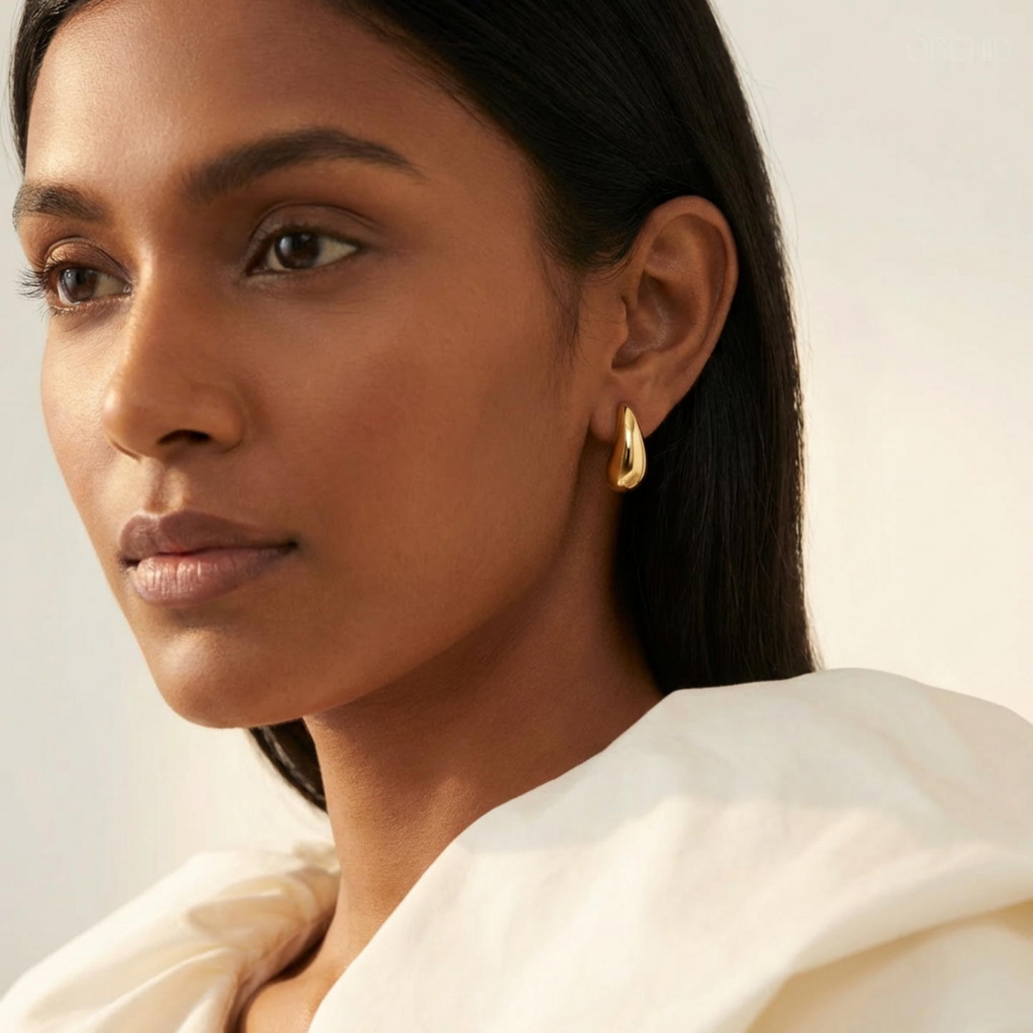 Woman wearing gold hoop earrings with a neutral background
