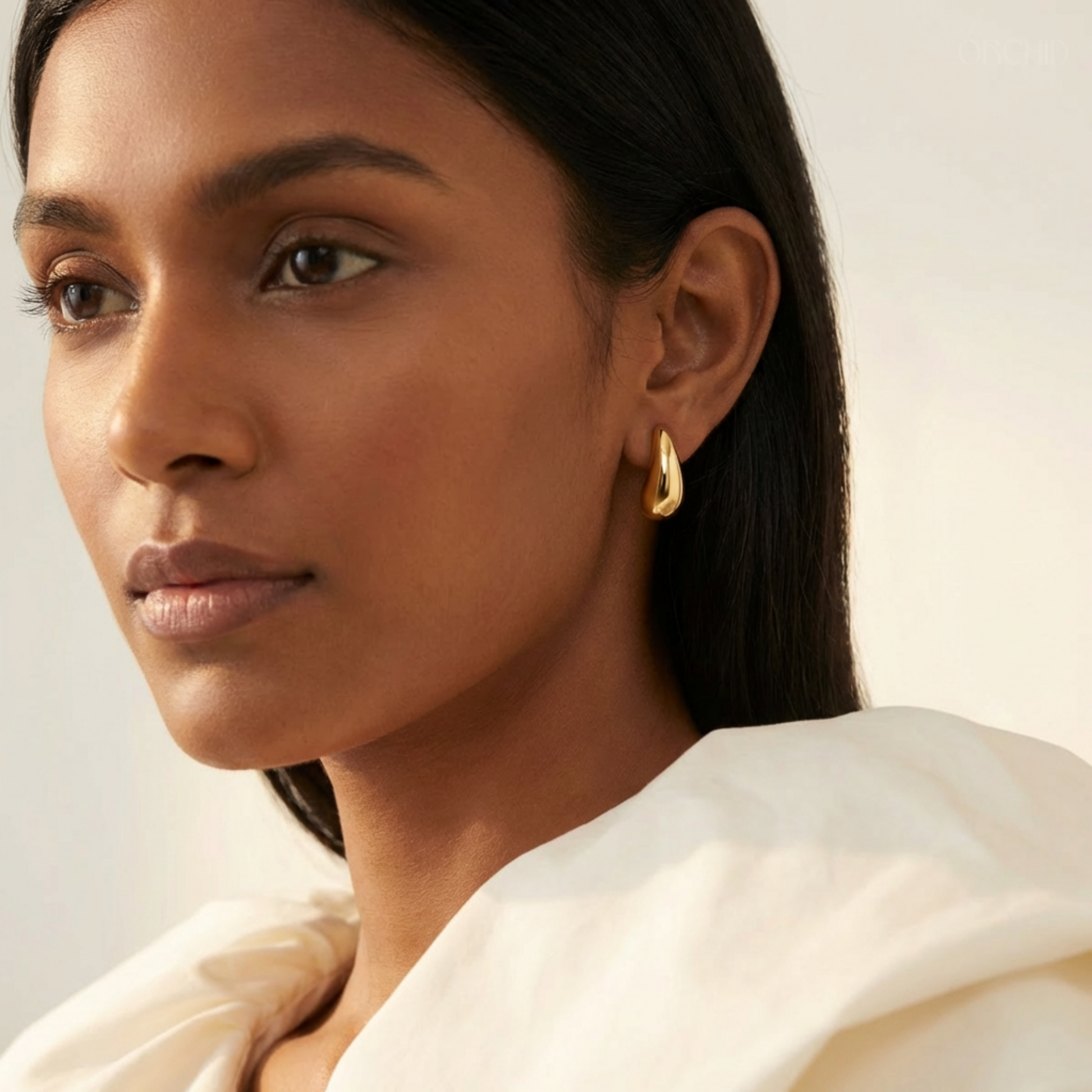 Woman wearing gold hoop earrings with a neutral background