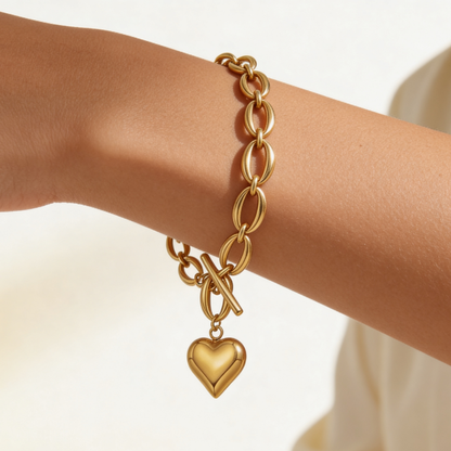 Gold chain bracelet with a heart charm on a wrist against a neutral background