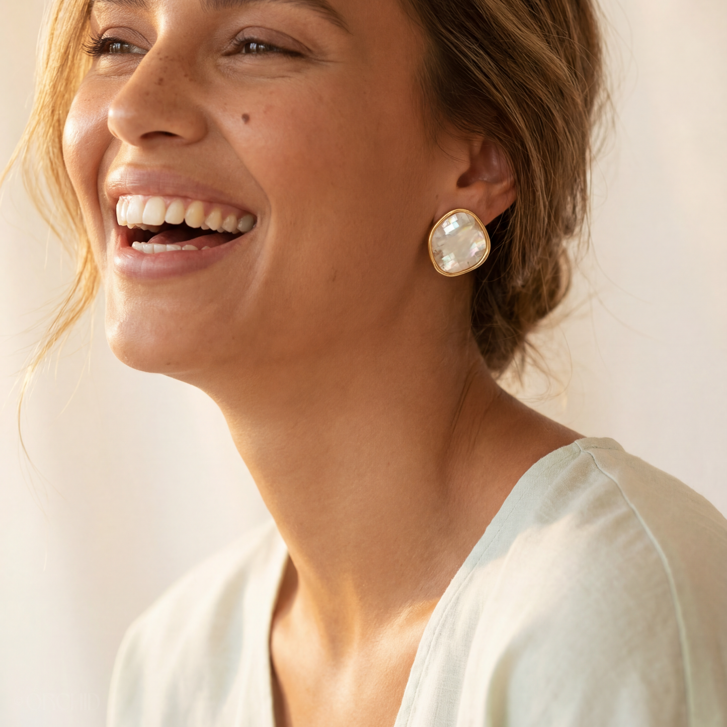 Woman wearing gold earrings with a plain background