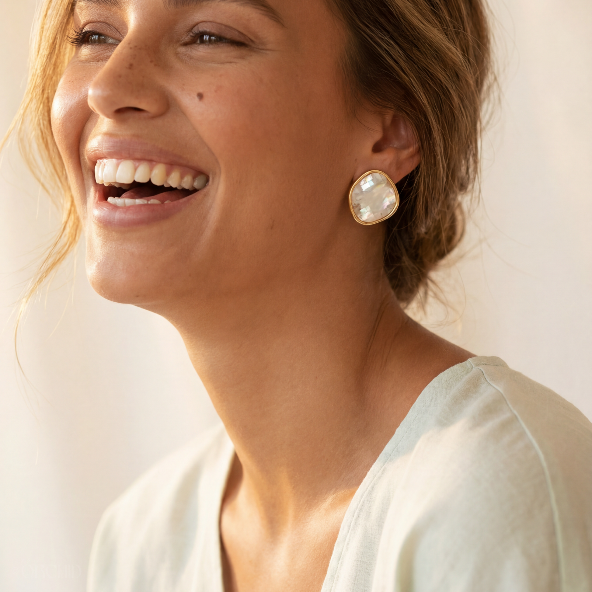 Woman wearing gold earrings with a plain background