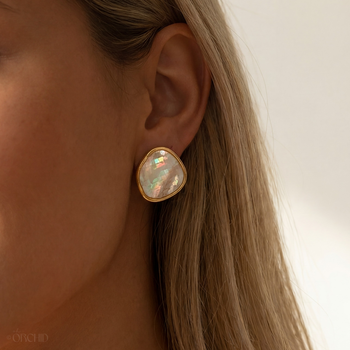 Close-up of a gold earring with a gemstone worn by a person with blonde hair.