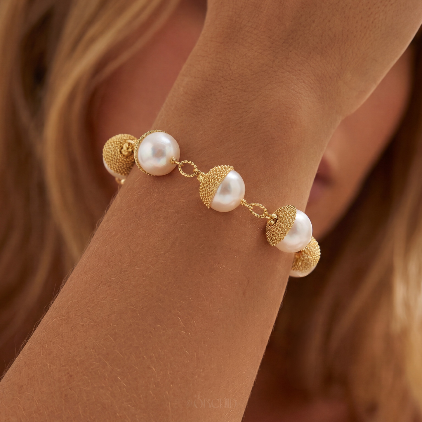 Gold and pearl bracelet on a wrist with a blurred background