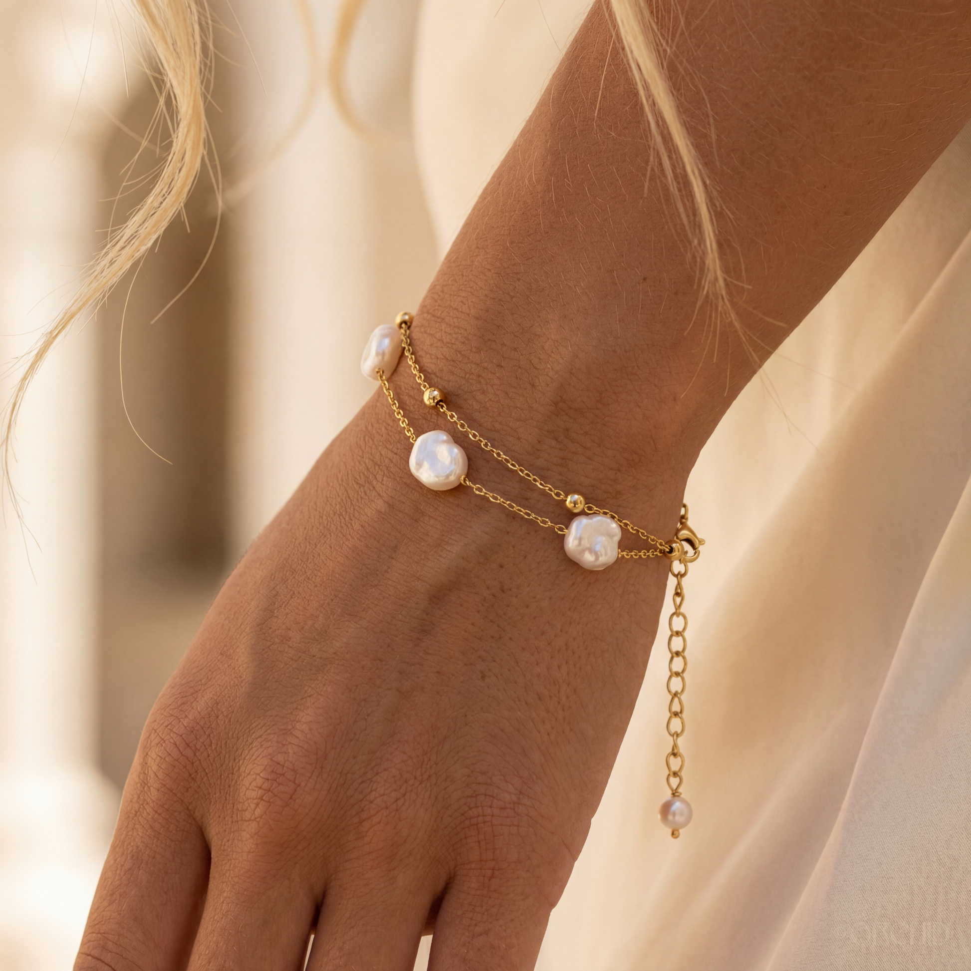 Gold bracelet with pearl beads on a wrist against a neutral background