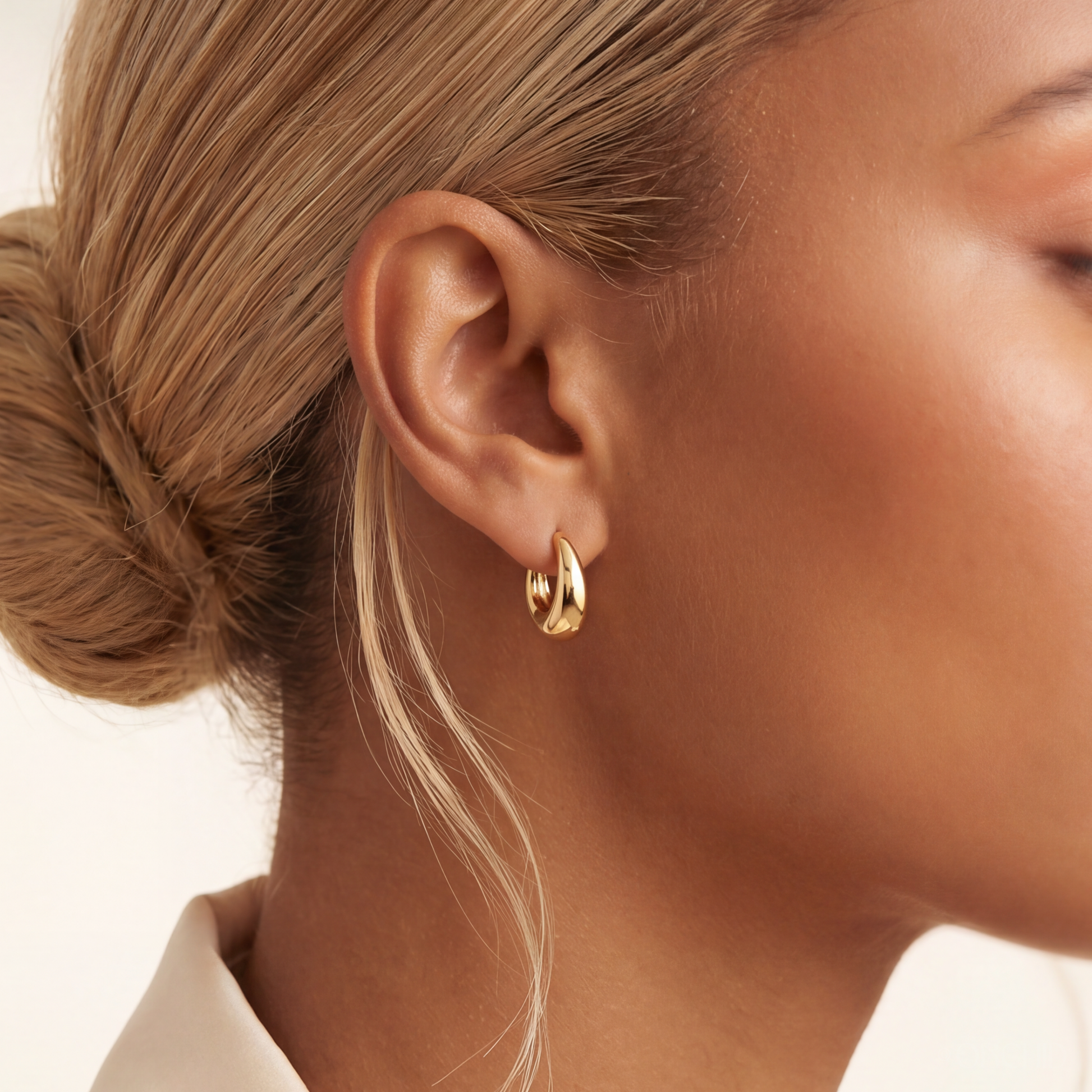Close-up of a person wearing gold hoop earrings with a neutral background