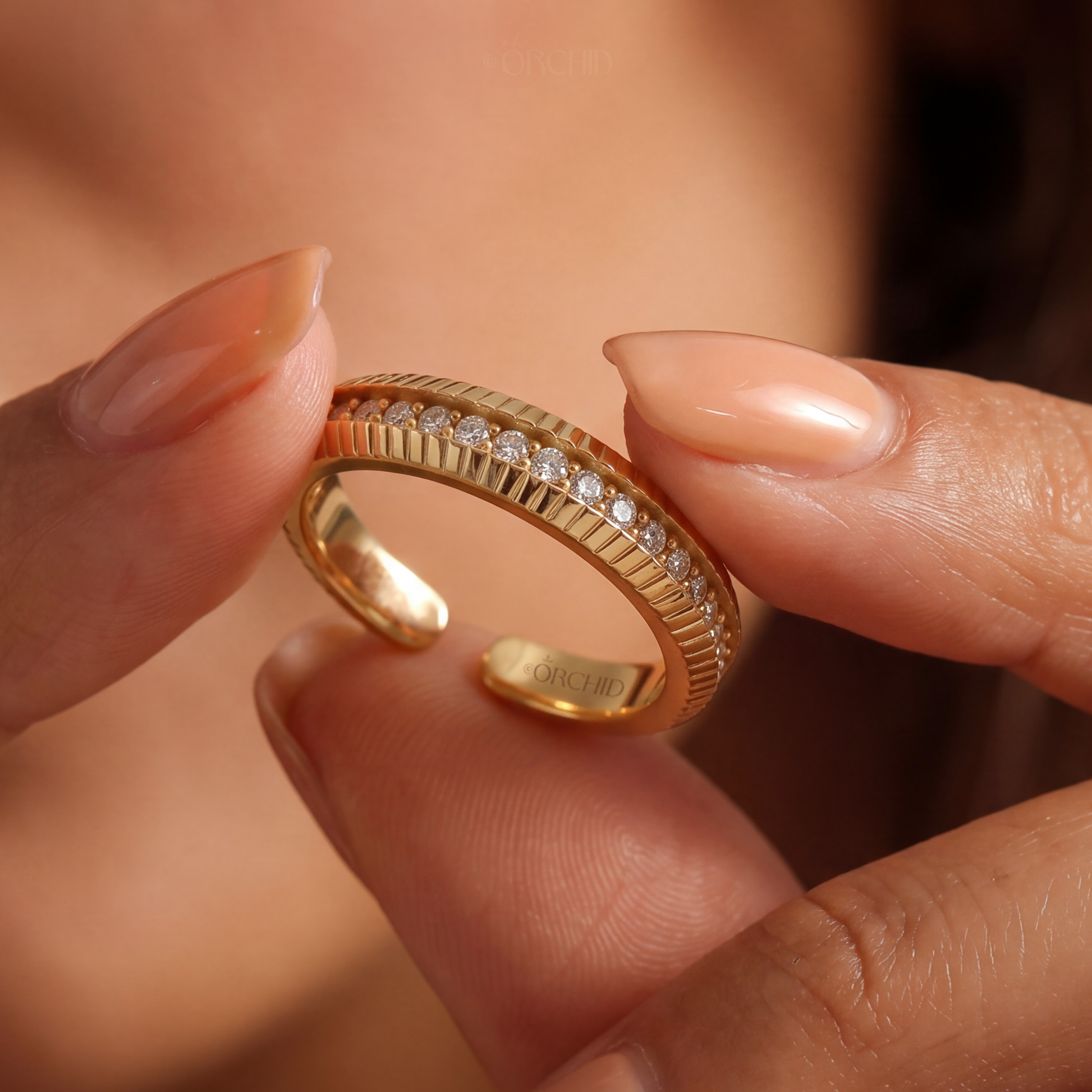 Gold ring with diamonds held between fingers against a blurred background
