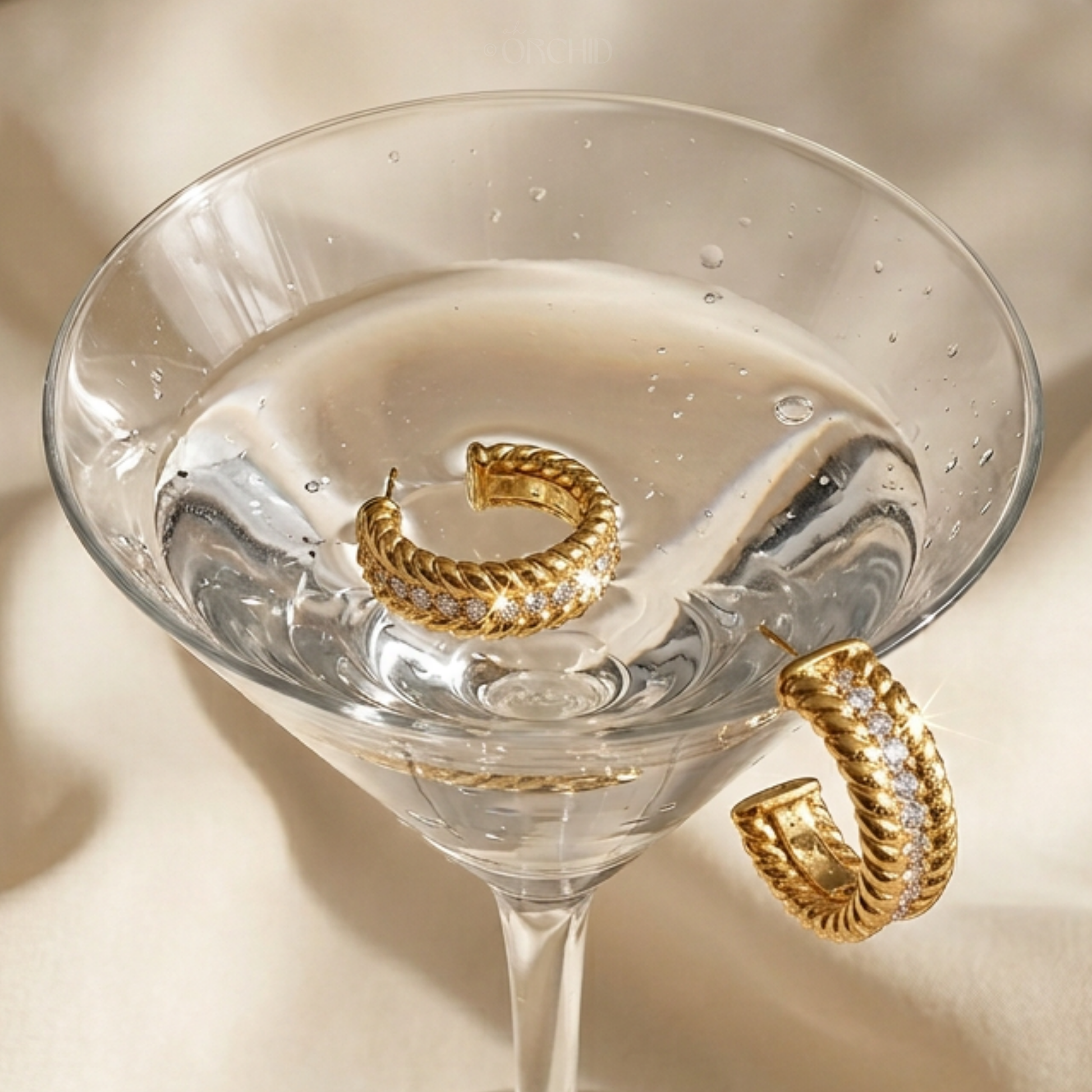 Gold hoop earrings in a martini glass on a beige background