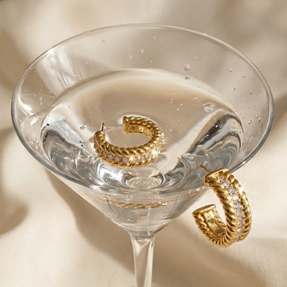 Gold hoop earrings in a martini glass on a beige background