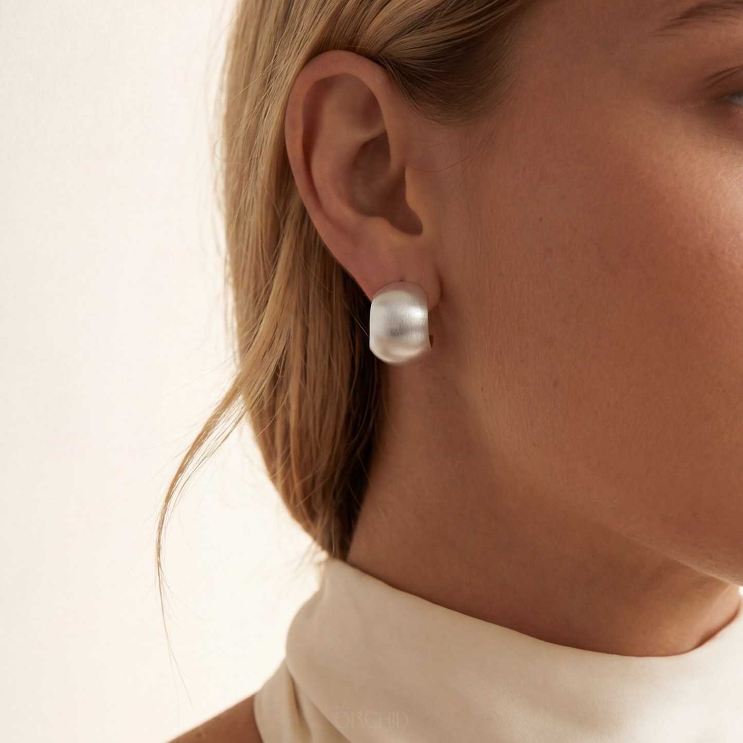 sterling silver hoop earrings worn by a person with a neutral background
