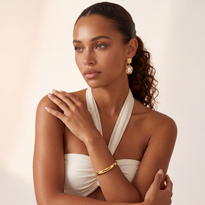 Woman wearing a white dress with gold jewelry against a beige background