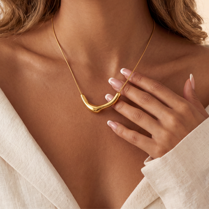 Gold necklace being worn with a hand adjusting it, on a neutral background