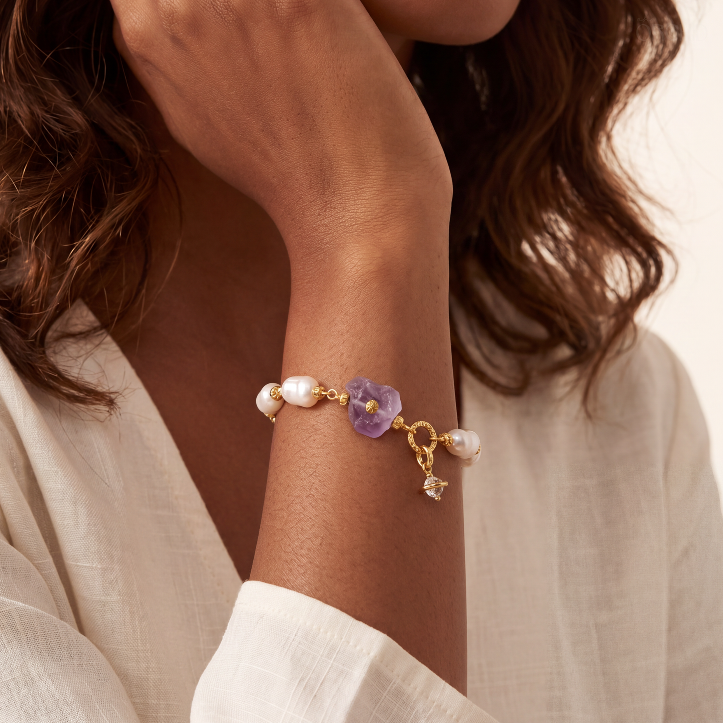 Bracelet with purple amethyst charm and pearls on a wrist, with a neutral background