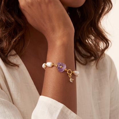 Bracelet with purple amethyst charm and pearls on a wrist, with a neutral background