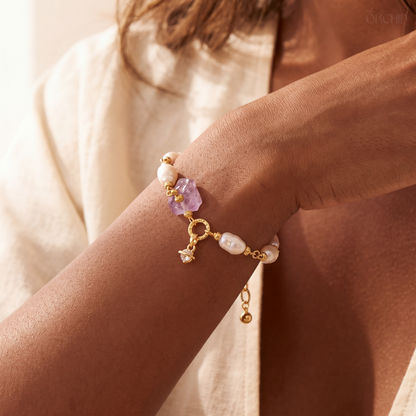 Close-up of a wrist wearing a delicate bracelet with pearls and a purple gemstone.