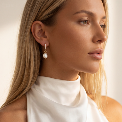 Close-up of a woman wearing pearl earrings with a neutral background