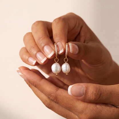 Hand holding a pair of pearl earrings against a neutral background