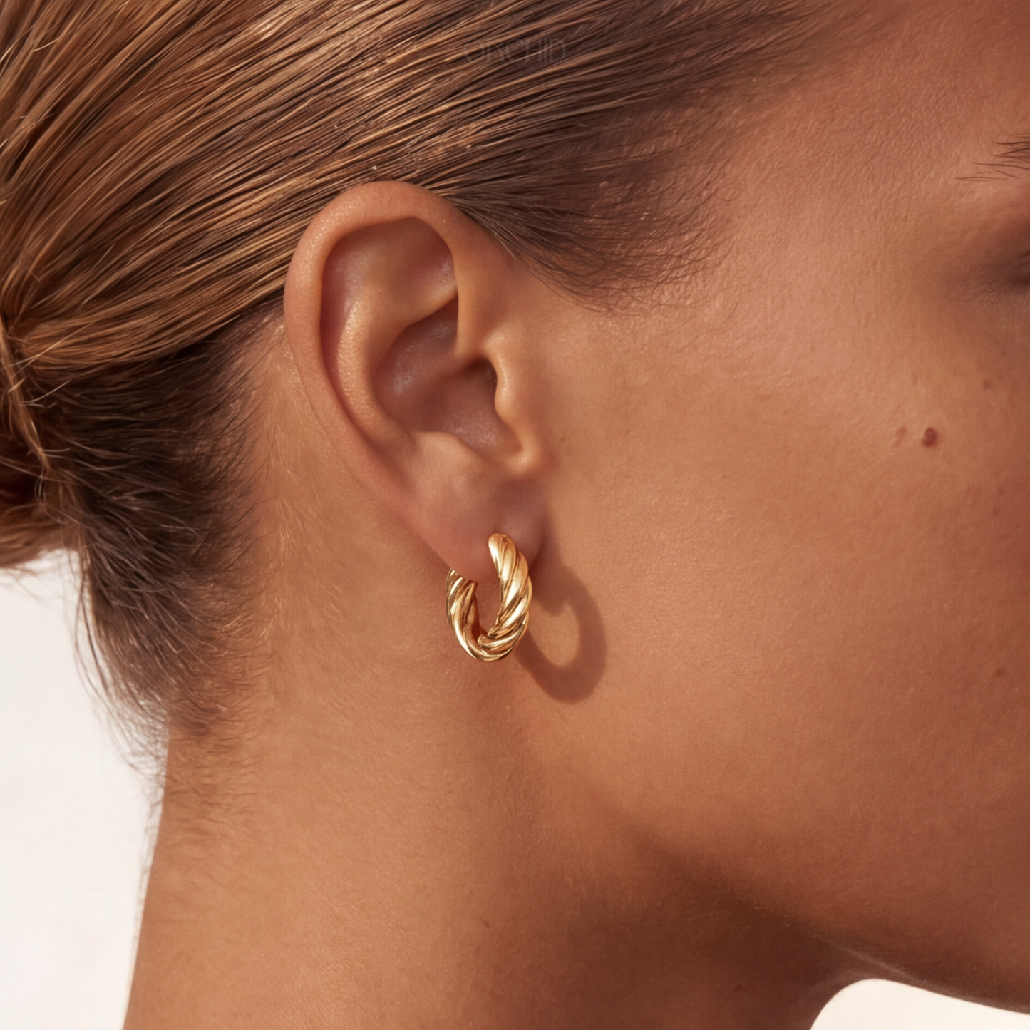 Gold hoop earring worn by a person with a neutral background
