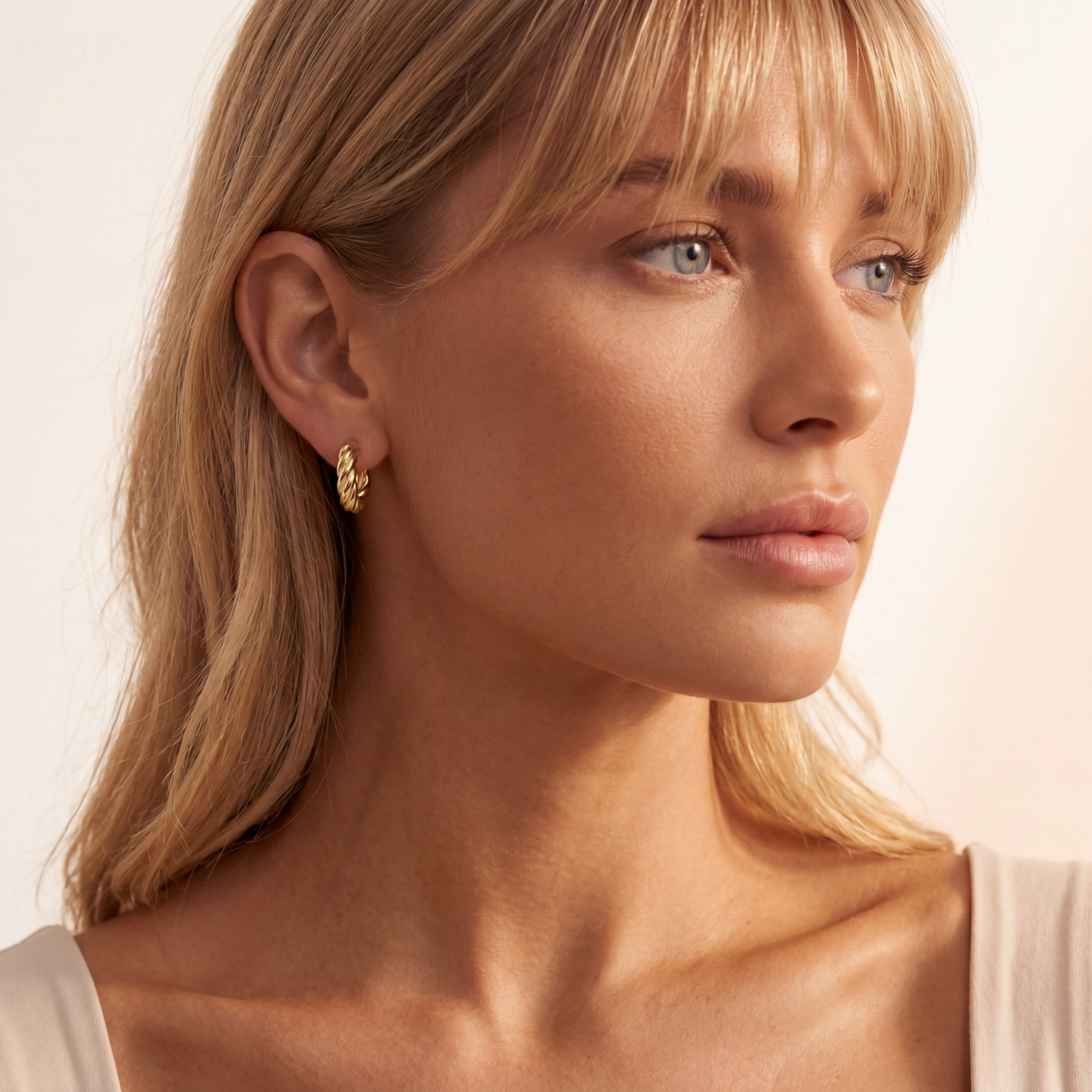 Close-up of a woman wearing gold earrings with a neutral background