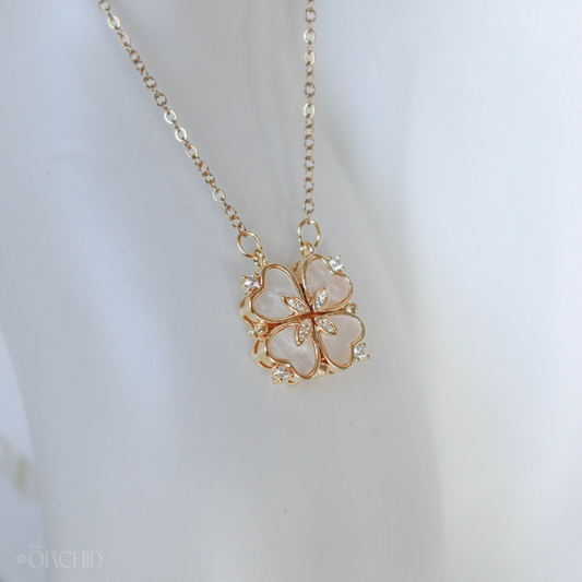 Gold necklace with a clover-shaped pendant on a light background