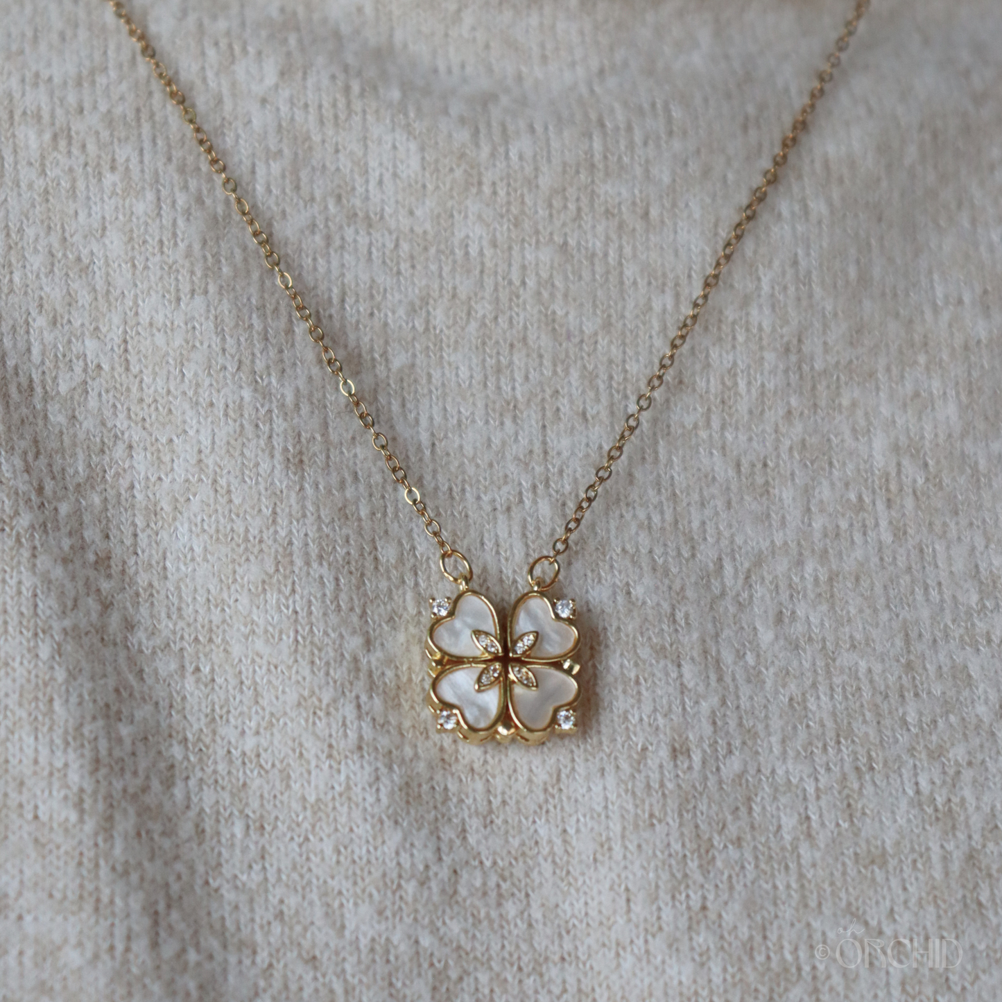 Gold necklace with a four-leaf clover pendant on a beige fabric background