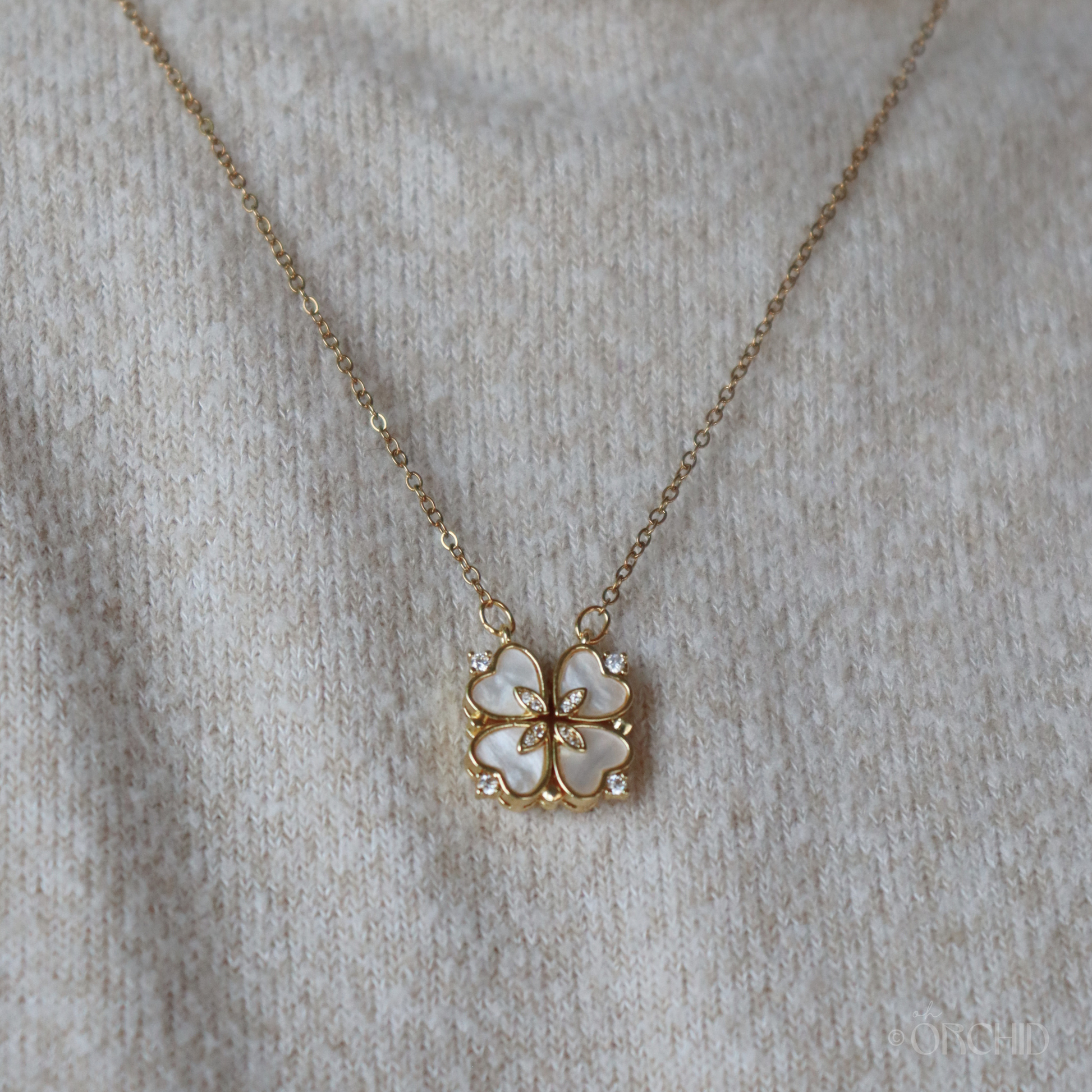 Gold necklace with a four-leaf clover pendant on a beige fabric background